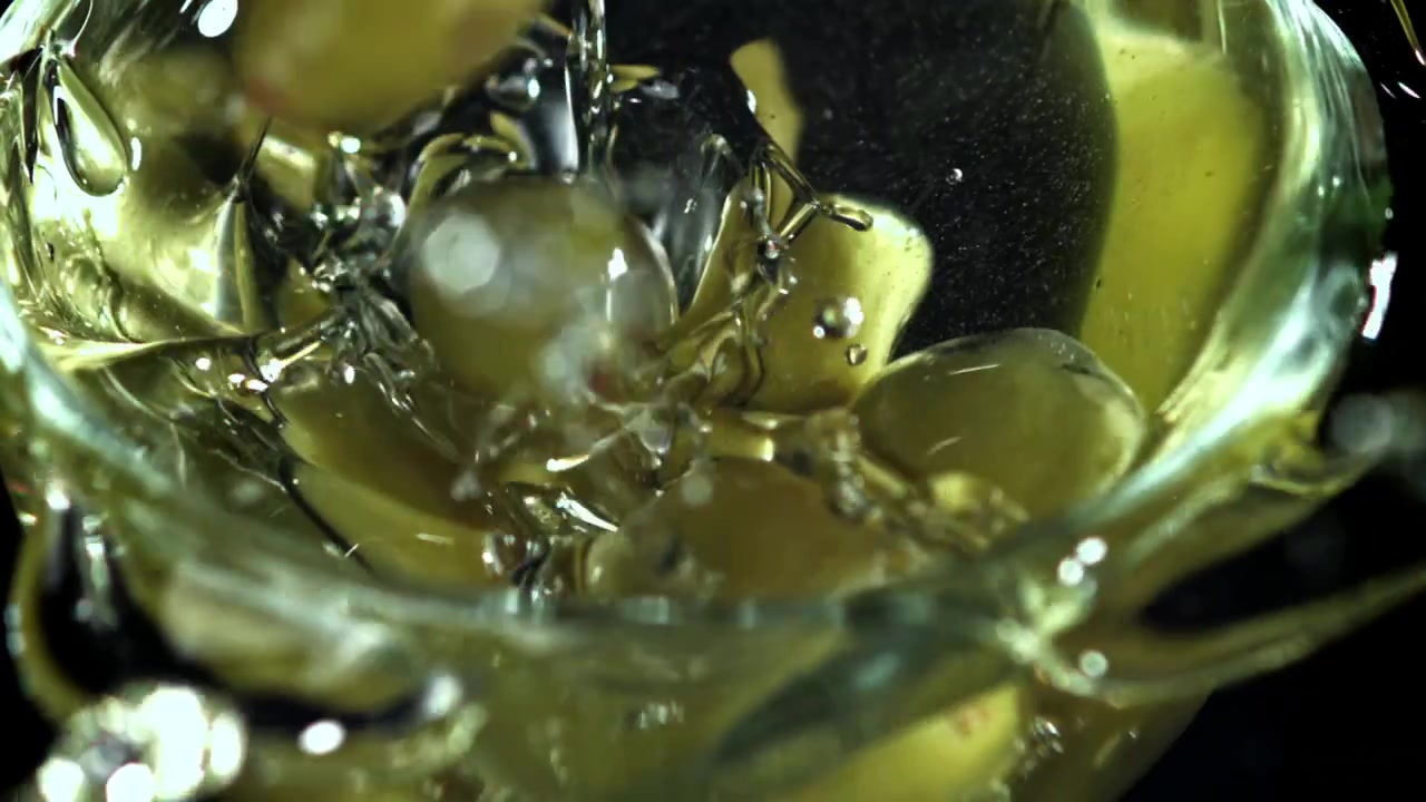 Olive verdi che cadono e schizzano in un liquido trasparente