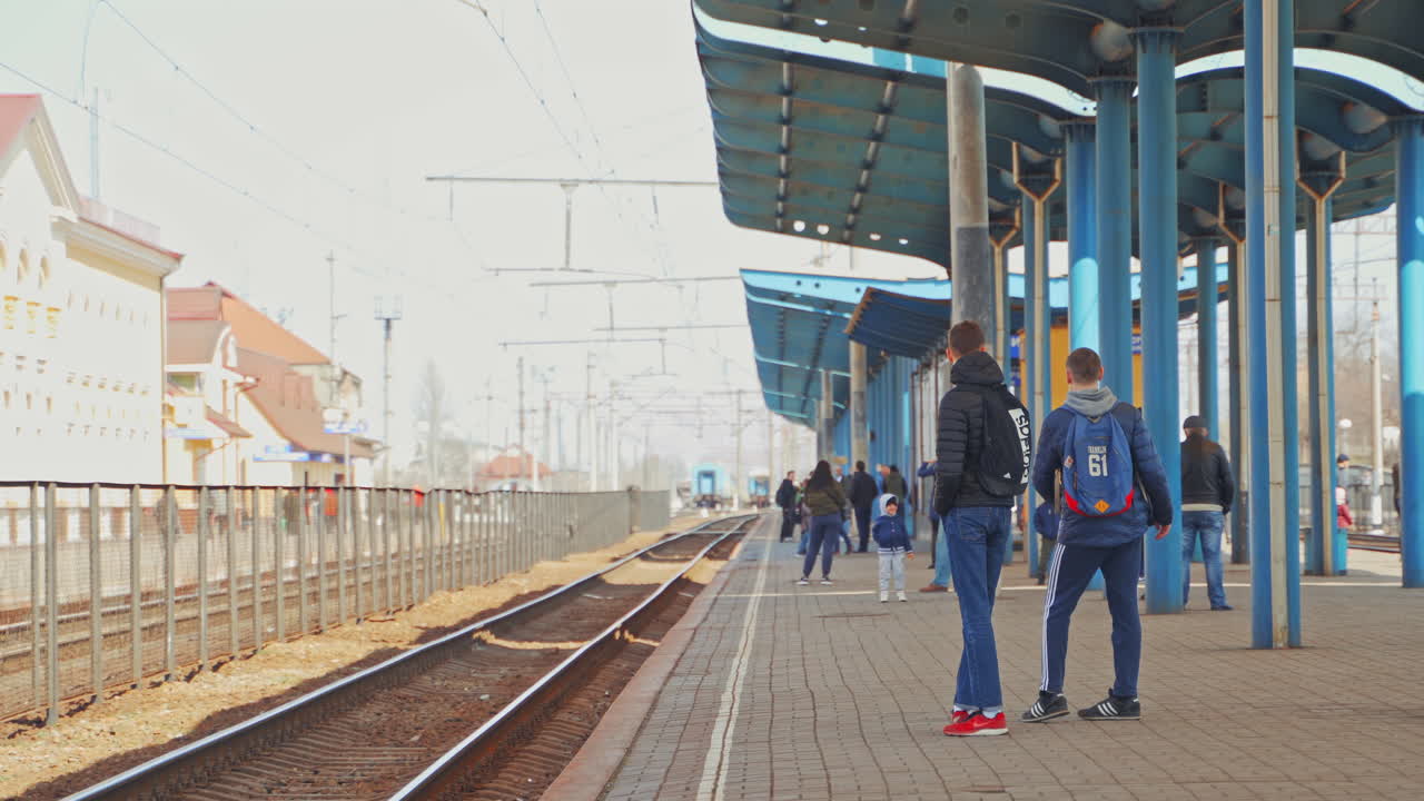Two teenagers standing on a railway platform waiting for a train. Young men in sportive clothes talking to each other on a railway station outdoors.