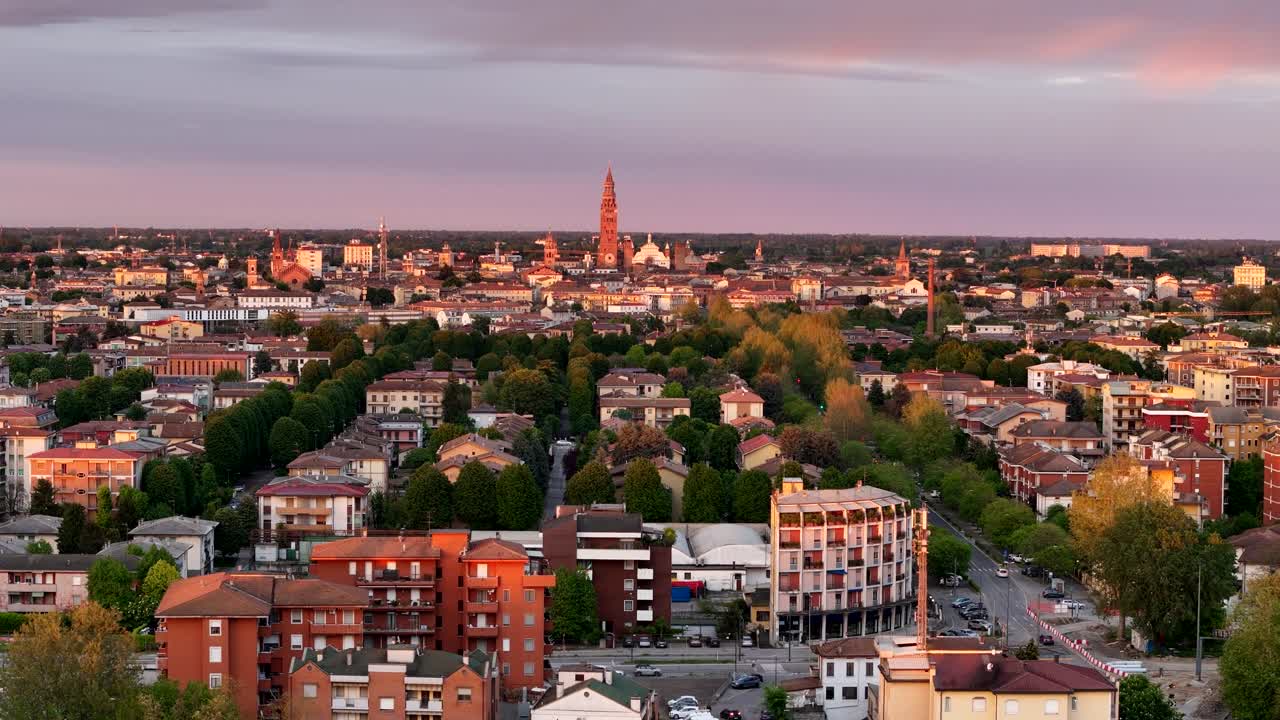 Aerial slow pull-away from the skyline of Cremona, Lombardy, featuring the Torrazzo di Cremona bell tower and cathedral bathed in warm sunset light
