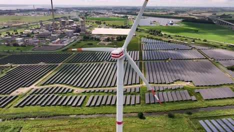A-wind-turbine-standing-in-a-solar-field,-generating-renewable-energy,-drone-orbit,-green-fields,-parallax-effect