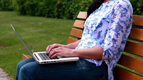 mujer sentada en un banco del parque usando una computadora portátil