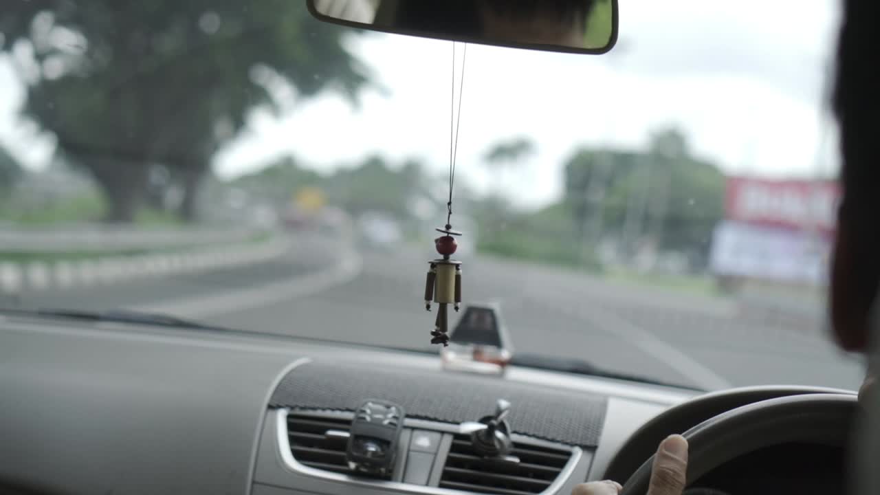 Car cruising down road in Jakarta, Indonesia with minifan hooked onto air-conditioner vent