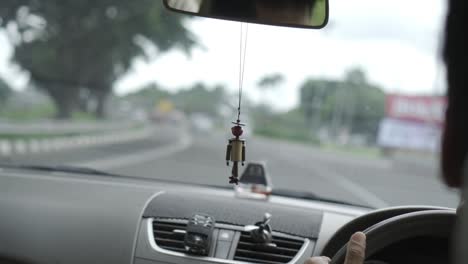 car cruising down road in jakarta, indonesia with minifan hooked onto air-conditioner vent