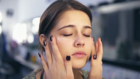 makeup artist applies concealer on the face of a young girl using her hands. she is also doing massage. base for perfect makeup