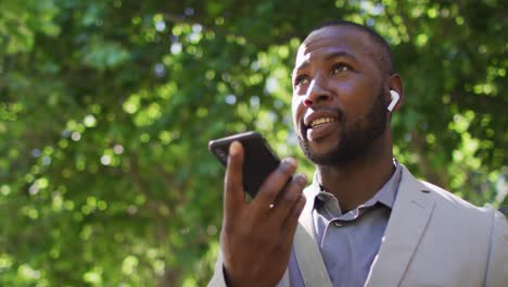 Portrait-of-happy-african-american-man-in-city-wearing-earphones-and-using-smartphone