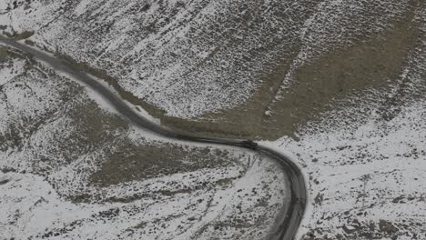 Toma-Aérea-De-Un-Auto-En-La-Calle-Con-Una-Montaña-Cubierta-De-Nieve-Al-Costado