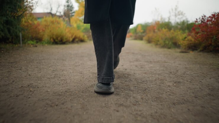 Close-up of feet in motion black jeans and canvas shoes jogging through a colorful autumn garden, capturing the essence of an active outdoor lifestyle amid fall scenery