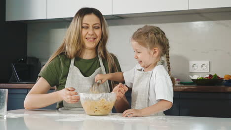 funny daughter plays with raw dough with mommy at table