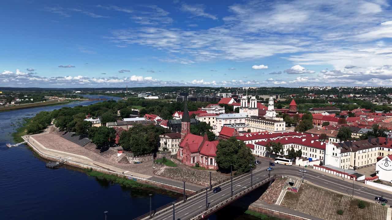Aerial view of Kaunas old town in Lithuania with historic churches, red rooftops, a riverfront, and a bridge under a vibrant summer sky
