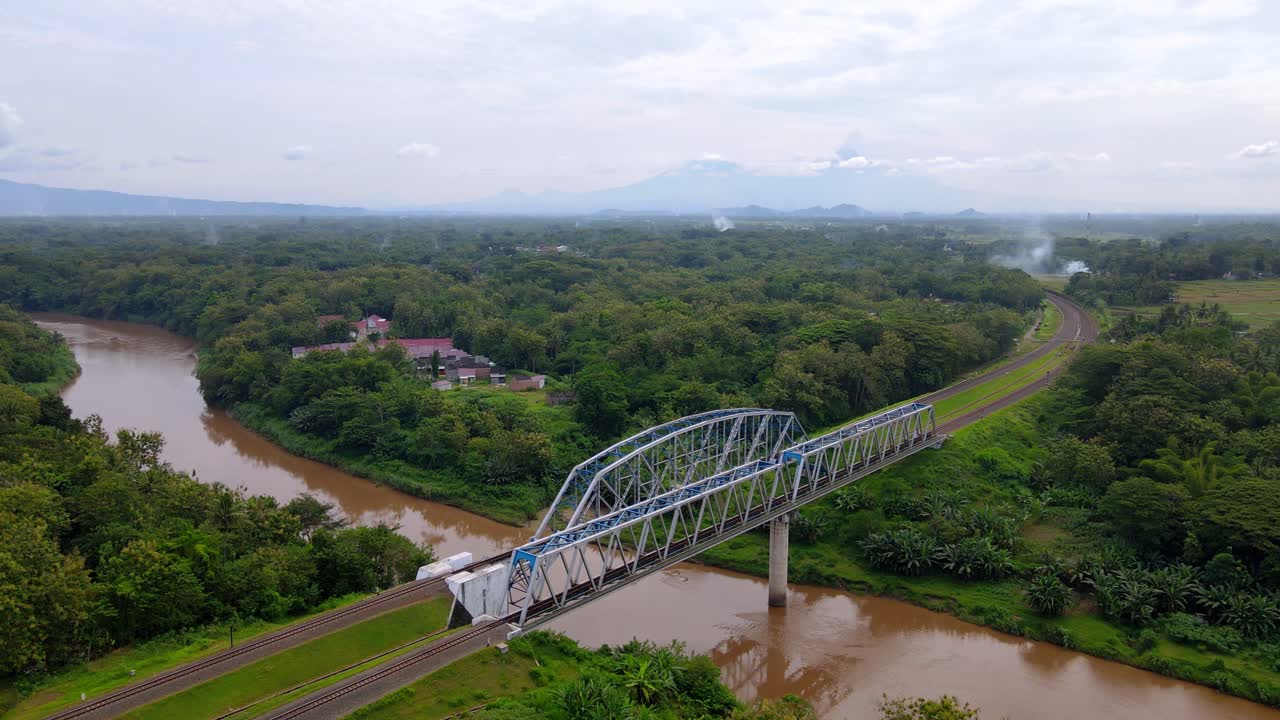 puente de tren que cruza el río sucio y conecta aldeas rurales en indonesia - vista aérea