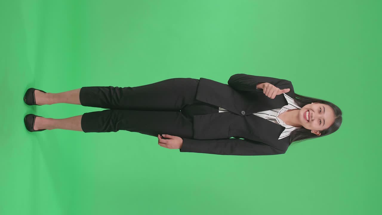 Full Body Of An Asian Business Woman Showing Thumbs Up Gesture And Smiling While Standing In The Green Screen Studio