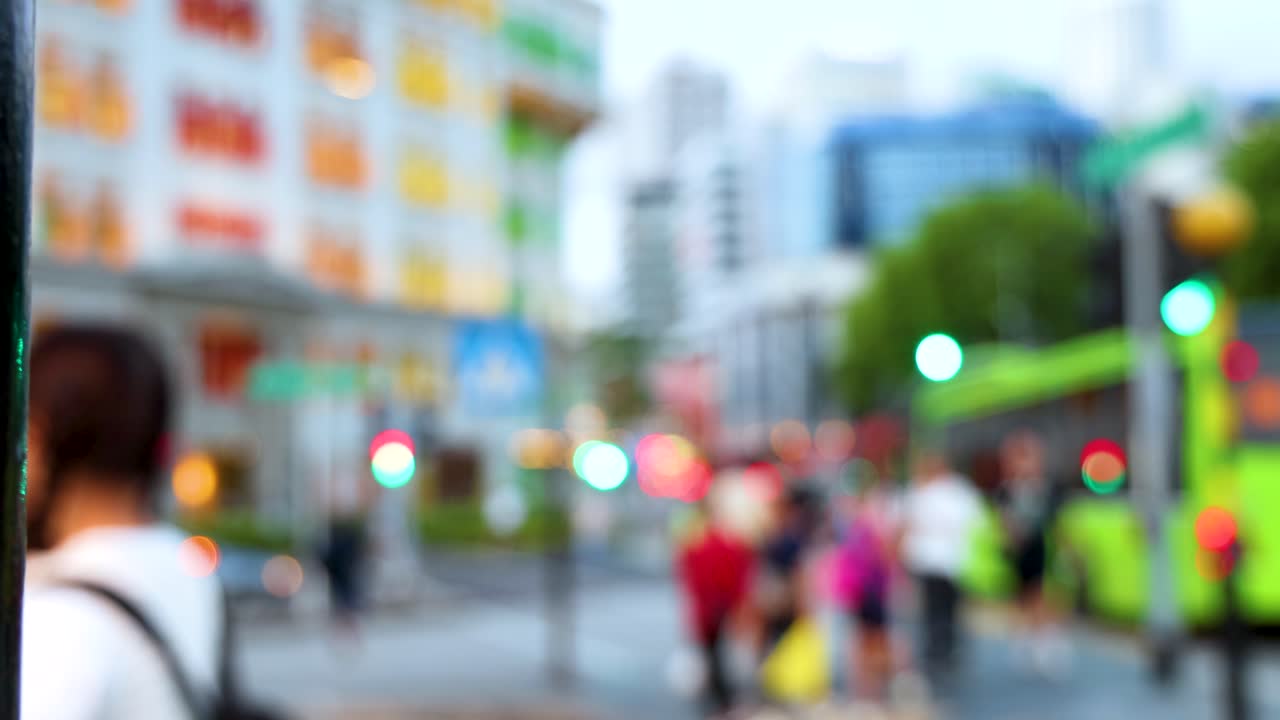 A group of people cross a busy city street in daylight, viewed from behind with a shallow depth of field and soft, colorful bokeh lighting
