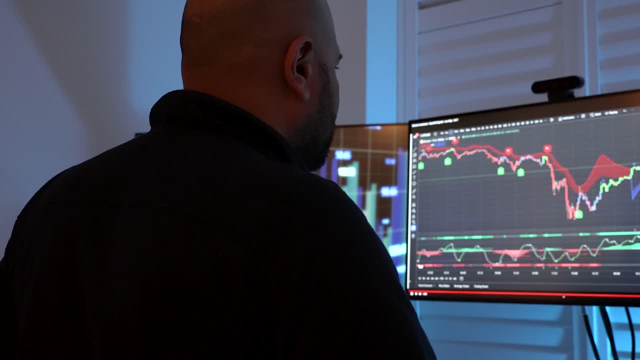 Man analyzing financial markets on dual monitors, blurred background, indoor, dusk light