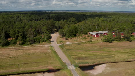 Aerial-ascending-footage-of-road-leading-to-forest.-Low-wooden-Nordic-buildings.-Cyclist-riding-on-road.-Denmark