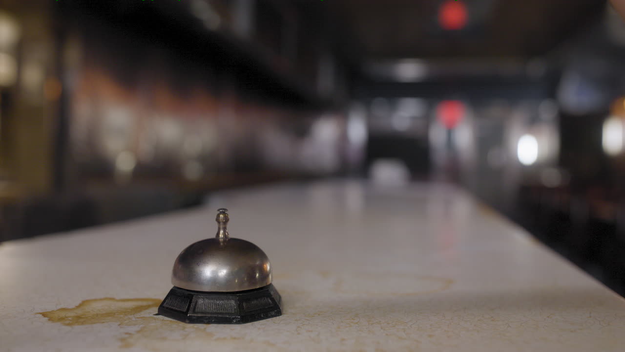 Close-up of a woman's hand ringing a call bell on a stained countertop at an old restaurant