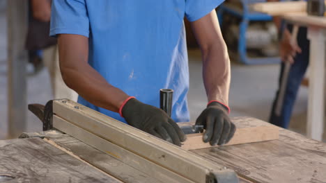 african american male colleagues guiding plank under table saw fence at woodshop, with push block