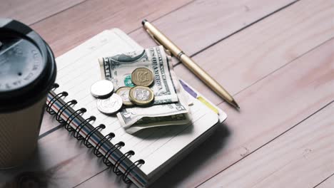 notebook with money, pen and coffee cup on wooden table