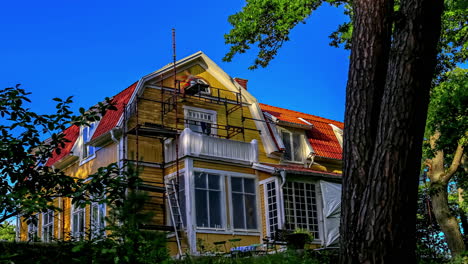 restoration work on retro vintage yellow house, scaffolding on house facade with front yard vegetation, time lapse