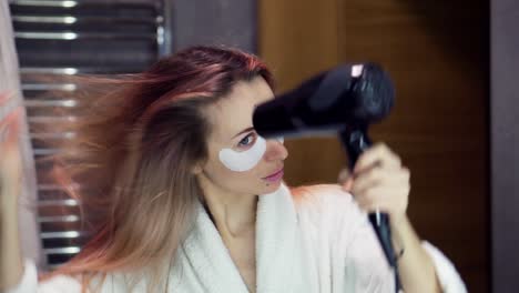 Confident-woman-looking-at-her-reflection-and-drying-her-hair-with-hair-dryer