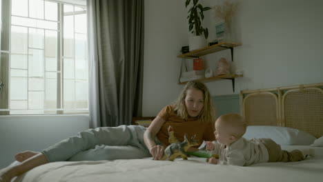 mother and baby playing with dinosaurs on a bed