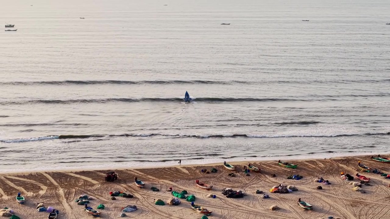 Vista aerea che mostra barche da pesca che riposano su una spiaggia sabbiosa accanto a dolci onde marine vicino alla costa di Chennai durante una tranquilla giornata di sole, creando una scena di paesaggio costiero sereno.