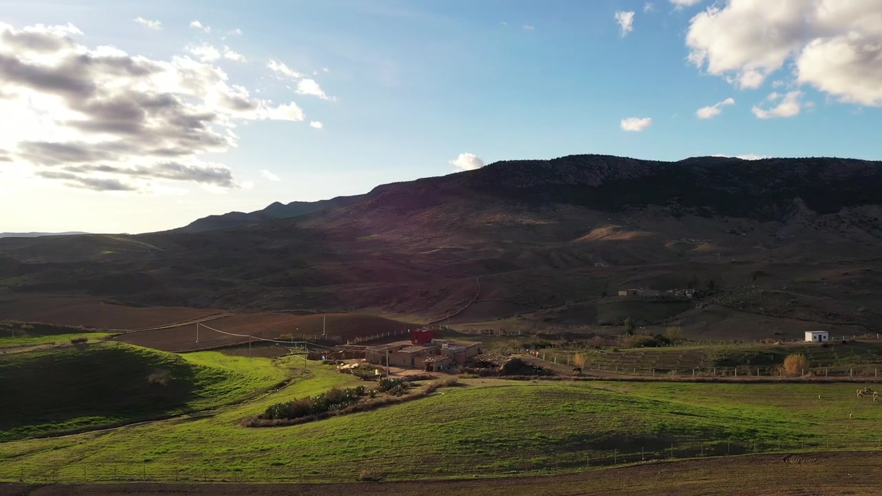 Imagens aéreas de drone de campos verdes de planalto e assentamentos rurais sob uma dramática cadeia de montanhas no Médio Atlas, Marrocos, ideais para projetos de viagens, agricultura e documentários