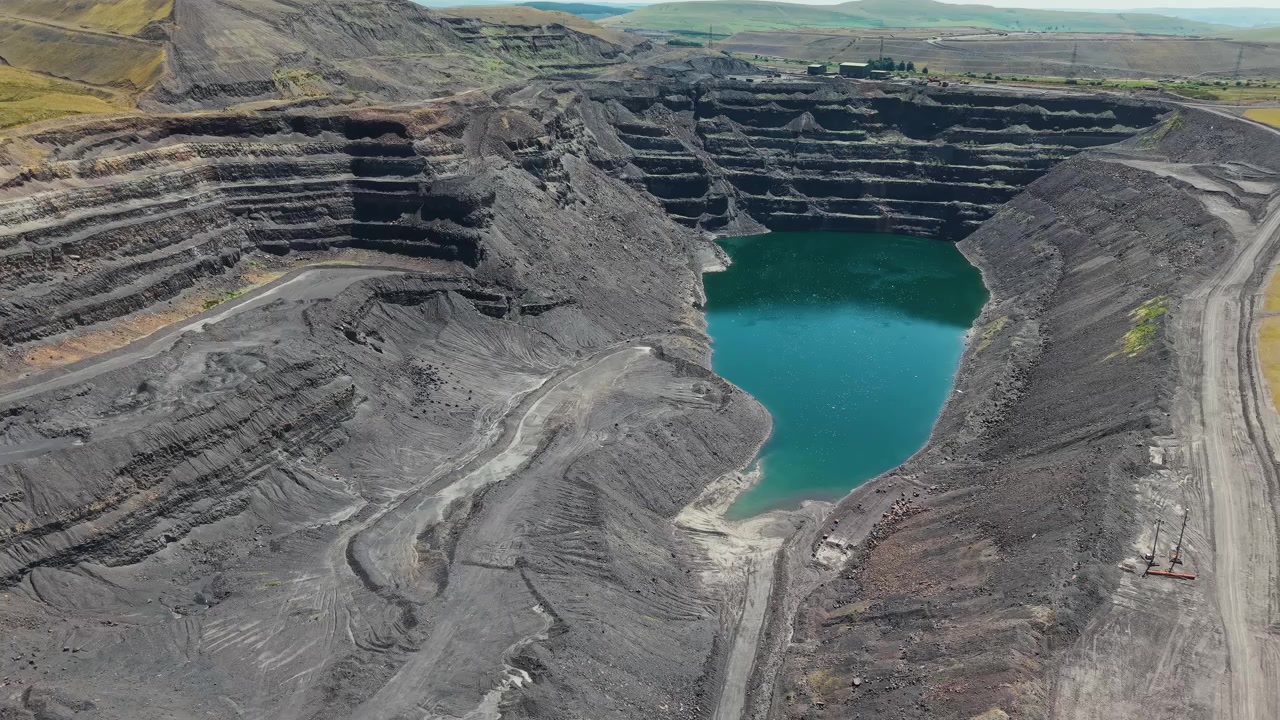 Disused surface coal mine crater showing steep rock benches and flooded pit bottom, open pit mining environmental impact across surrounding landscape