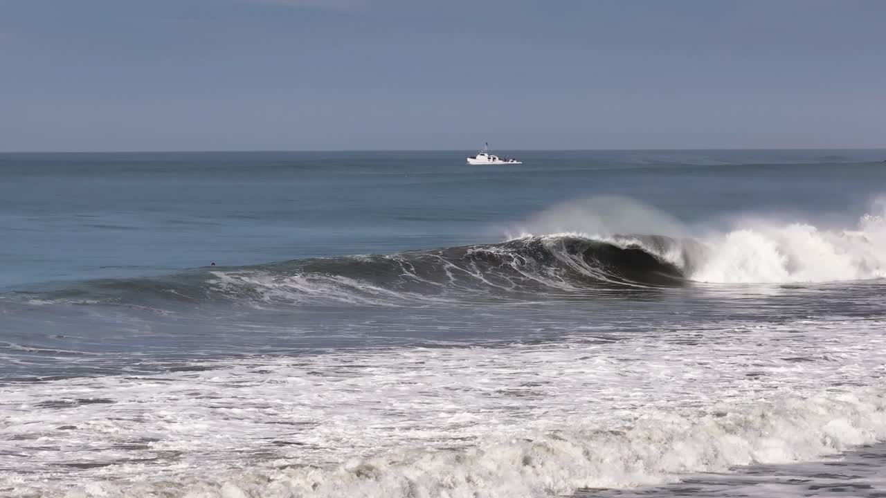 barreling waves with a white boat in the distance