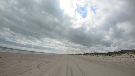 POV-thru-windshield-of-vehicle-driving-on-deserted-beach-between-surf-and-dunes-of-North-Padre-Island-National-Seashore-in-Texas