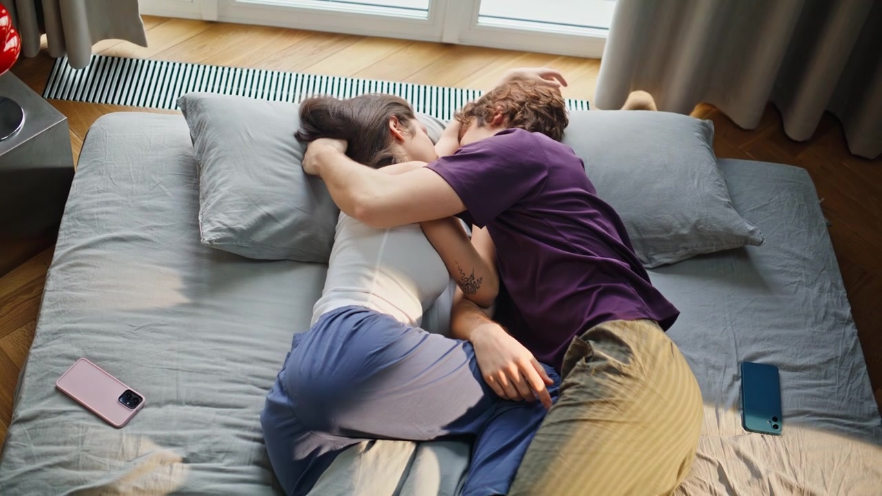 Students lying mattress enjoying cozy wake up top view. Pair reacting alarm