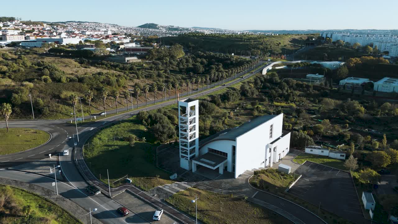Drone circles above Igreja Paroquial de Sao Bras in Amadora Portugal during sunrise, showing the church, surrounding buildings, and cityscape