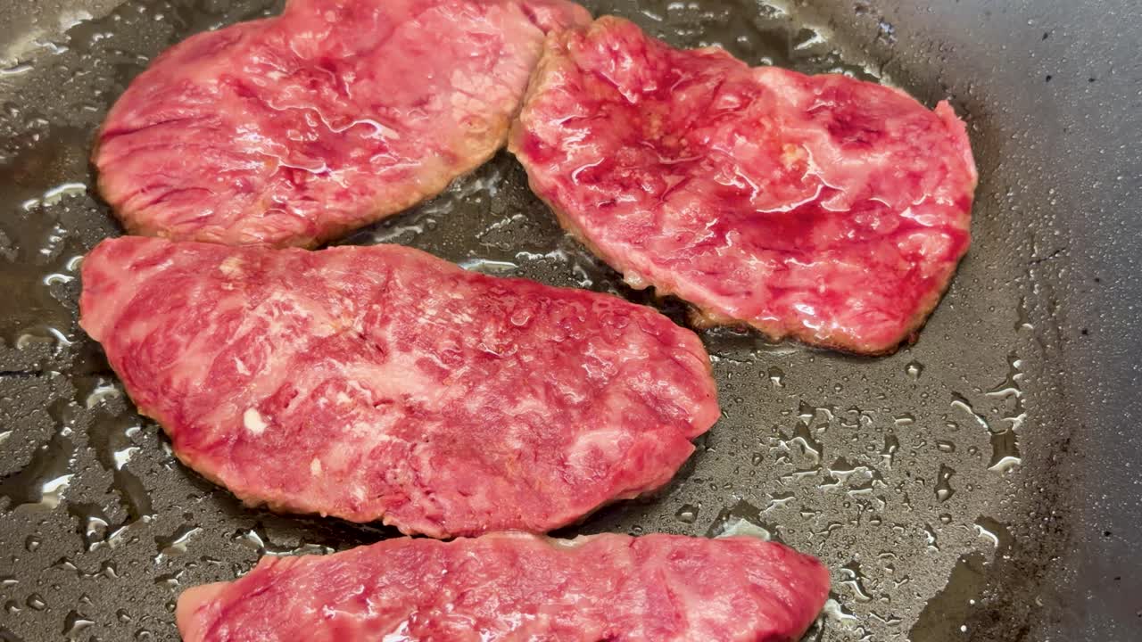 Primi piani di fette di manzo wagyu marmorizzato che sfrigolano in una padella calda durante la cottura.