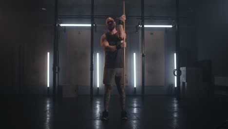 hombre haciendo ejercicios de estiramiento con un palo de madera en el gimnasio