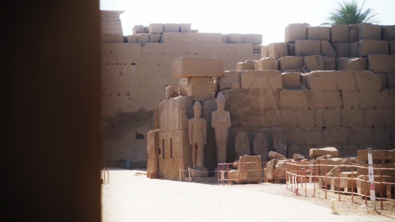Tourist path outside the Karnak Temple in Luxor, Egypt. Large rocks and tall statues with fences around.Sideways slide from behind a wall, low depth of field