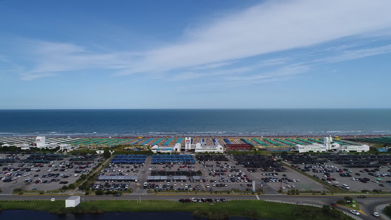 Pemandangan Udara Pantai Ramai dengan Payung, Tempat Parkir, dan Laut.