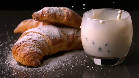 Strawberry-falling-in-glass-of-milk-beside-croissants