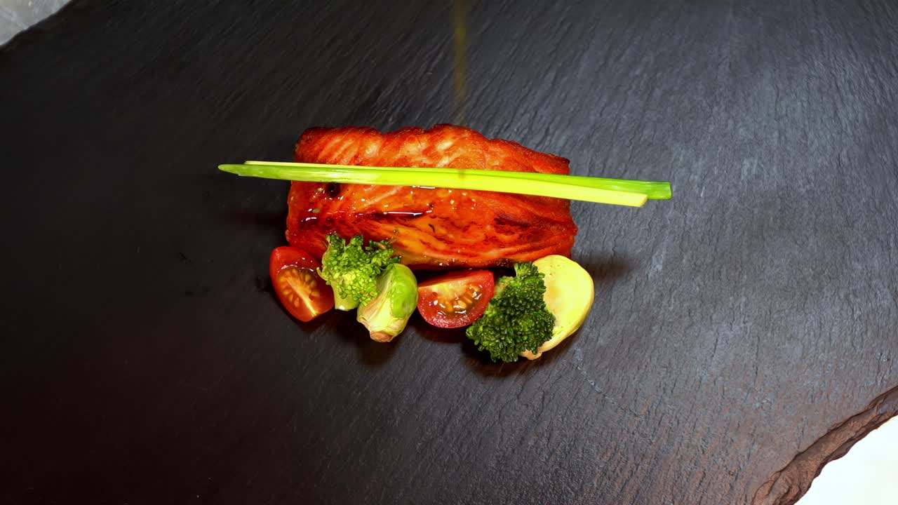 Artistic plating of grilled salmon filet with vegetables on black slate