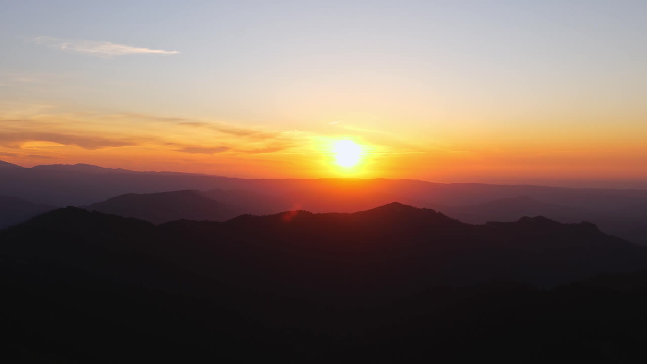 Transición de enfoque del sol poniente proyectando luz anaranjada y rojiza de la hora dorada, difuminando las montañas.