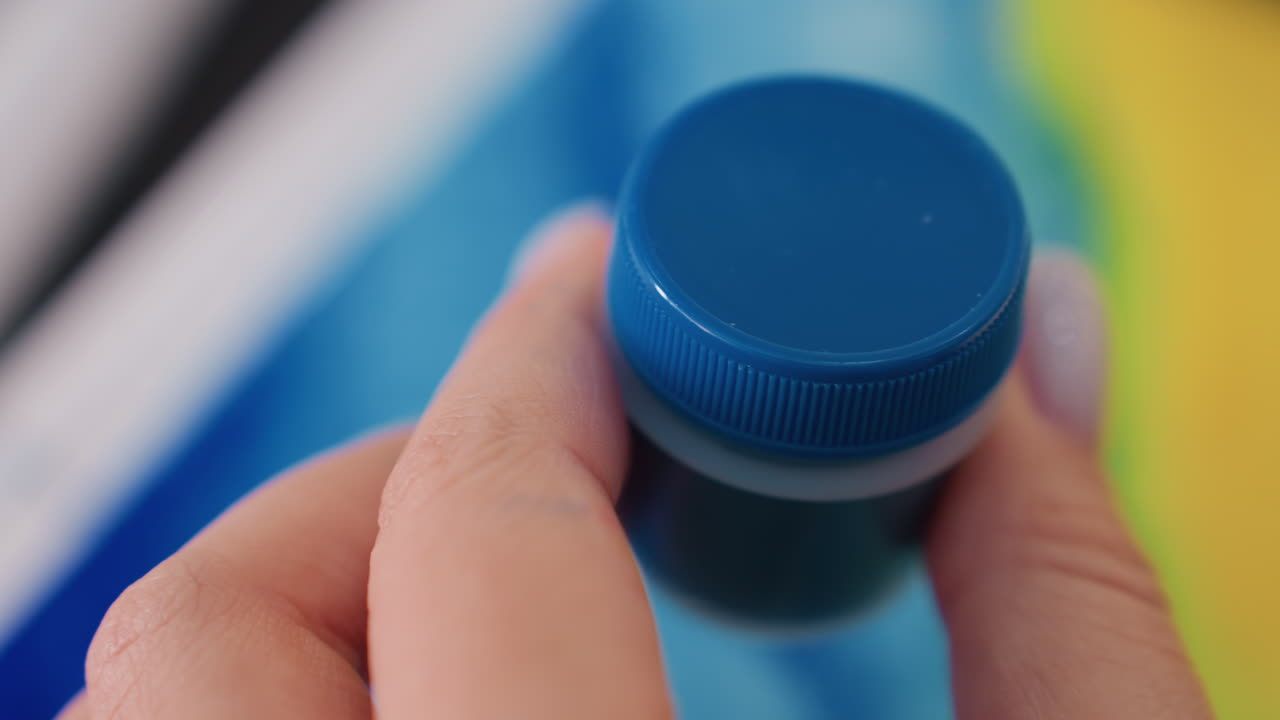Una donna chiude accuratamente un barattolo di vernice blu in modo sicuro; una donna meticolosa finisce di sistemare l'area di lavoro sigillando con cura un barattolo di vernice blu; una donna precisa sigilla con attenzione un barattolo di vernice blu per completare la pulizia