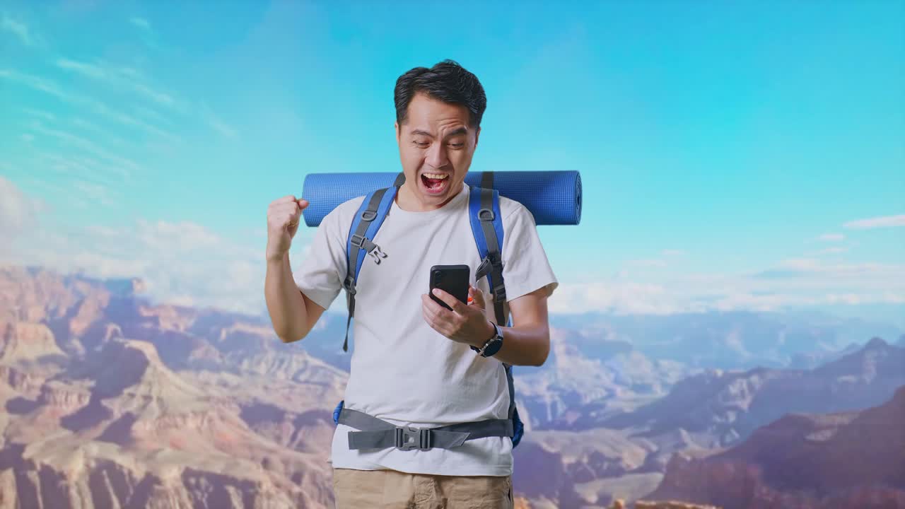 Asian Male Hiker With Mountaineering Backpack Looking At The Smartphone And Screaming Goal Celebrating The Success While Traveling At The Top Of Mountain