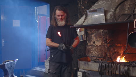 smiling blacksmith holds his red hot glowing candlestick in the making