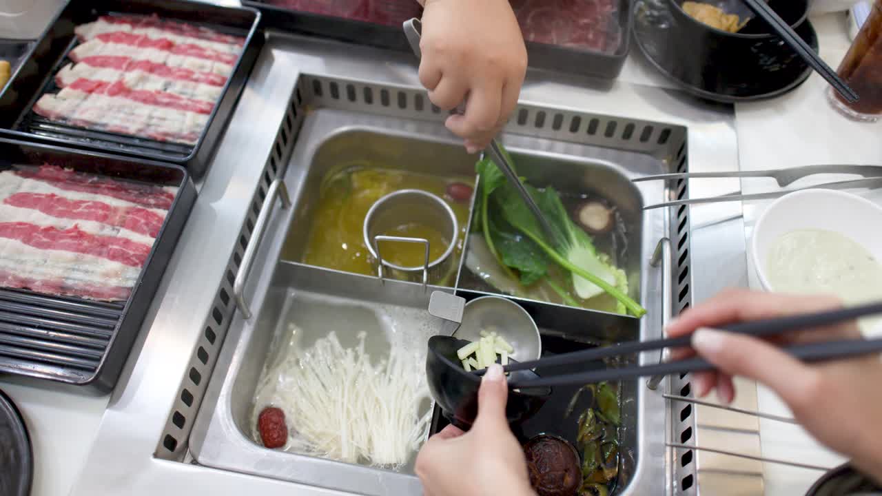 箸とトングを使って出汁の中で肉や野菜を調理している食事客の俯瞰ショット。