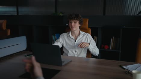 A-young-guy-with-curly-hair-in-a-white-shirt-shakes-hands-with-his-colleague-while-starting-a-business-communication-at-work-in-the-office