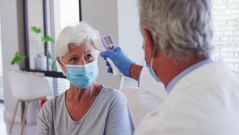 male caucasian doctor measuring temperature of senior caucasian woman at hospital