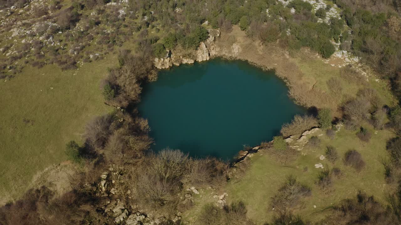estanque de montaña en la cordillera alta con agua esmeralda rodeado de laderas rocosas y árboles secos en albania