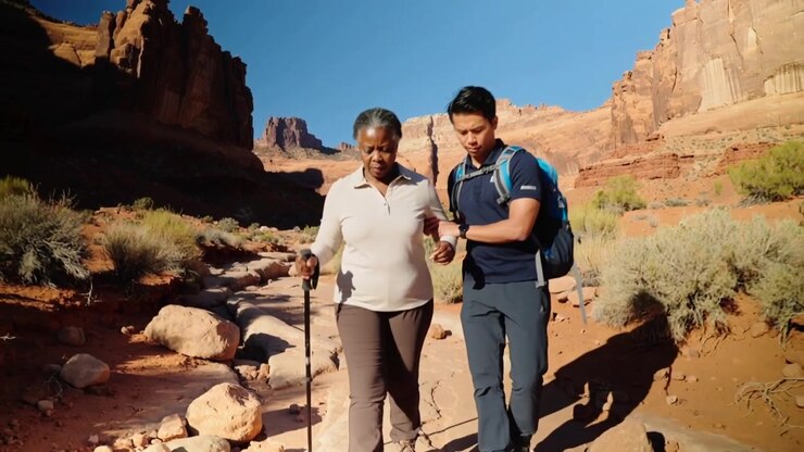 Planting trekking pole for balance, senior stepping while man navy polo holding arm on canyon trail