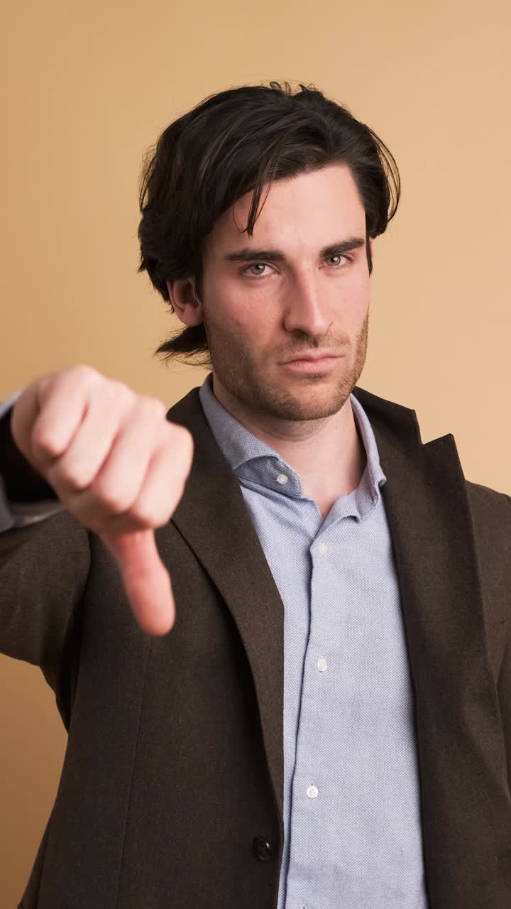 Upset businessman showing thumb down in brown studio