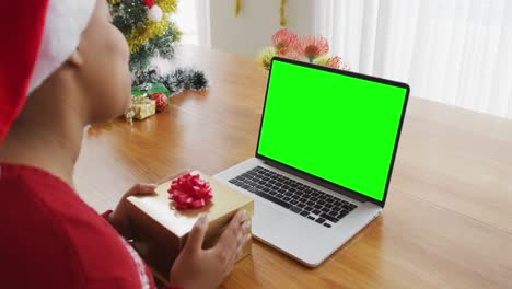 African-american-woman-with-present-making-laptop-christmas-video-call,-with-green-screen-copy-space