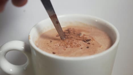 putting spoon of hot chocolate powder into mug of hot milk and stirring