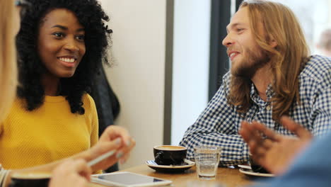 close-up view of multiethnic group of friends laughing and drinking coffee sitting at a table in a cafe